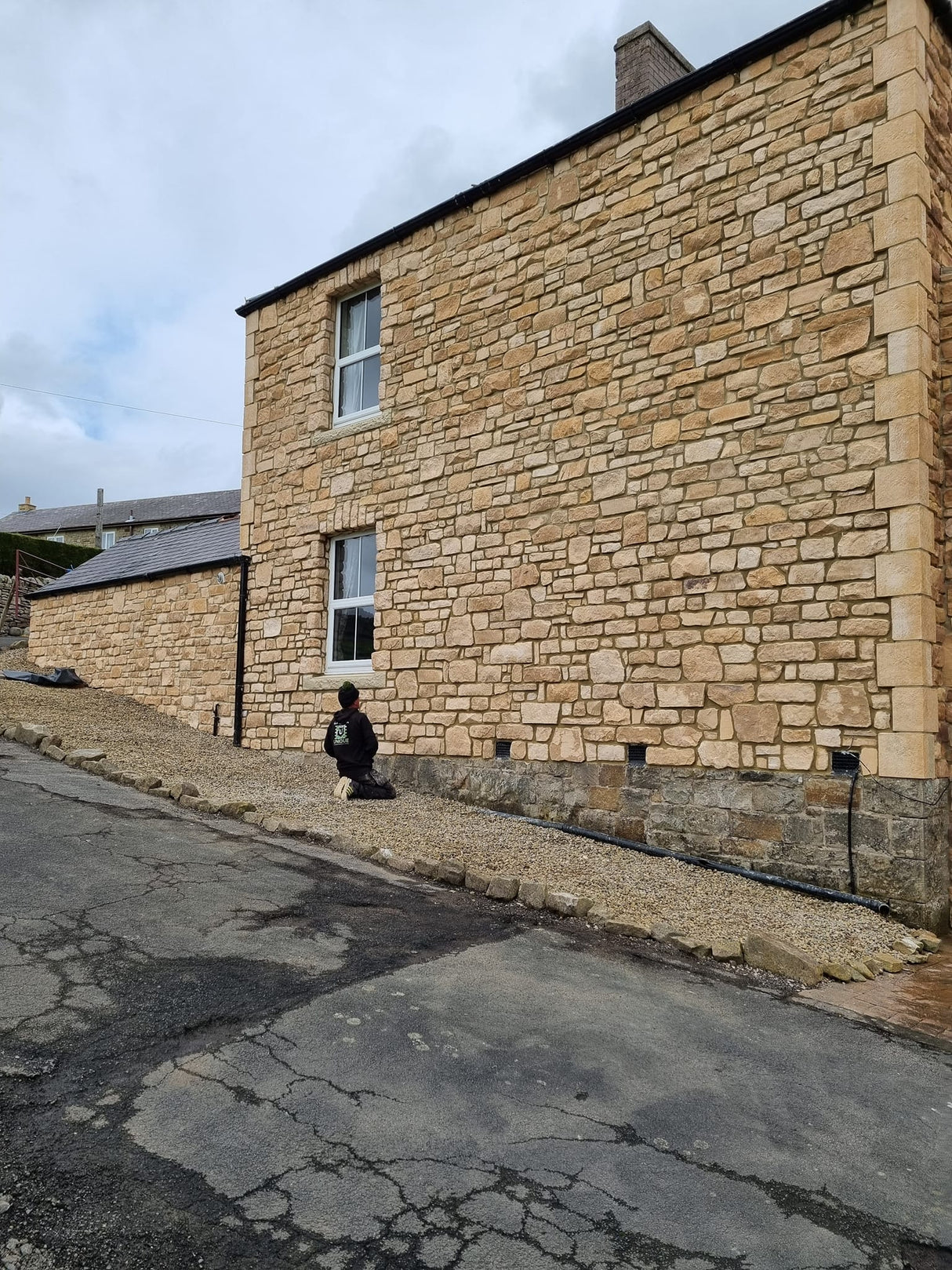 Exterior view of a building showcasing Burnt Buff Blend Stone Cladding with a worker preparing the area.