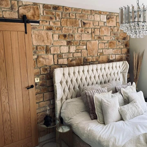 Cozy bedroom featuring Burnt Buff Blend stone cladding wall, elegant bed, and stylish decor accents.