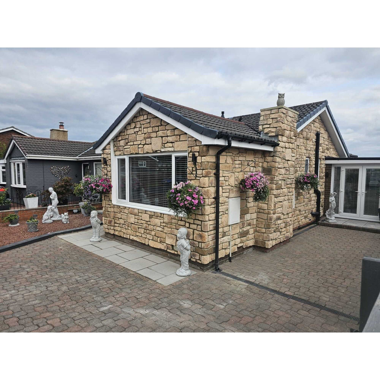 Stone-clad house exterior with flower pots and garden sculptures, showcasing beautiful Stone Cladding design.