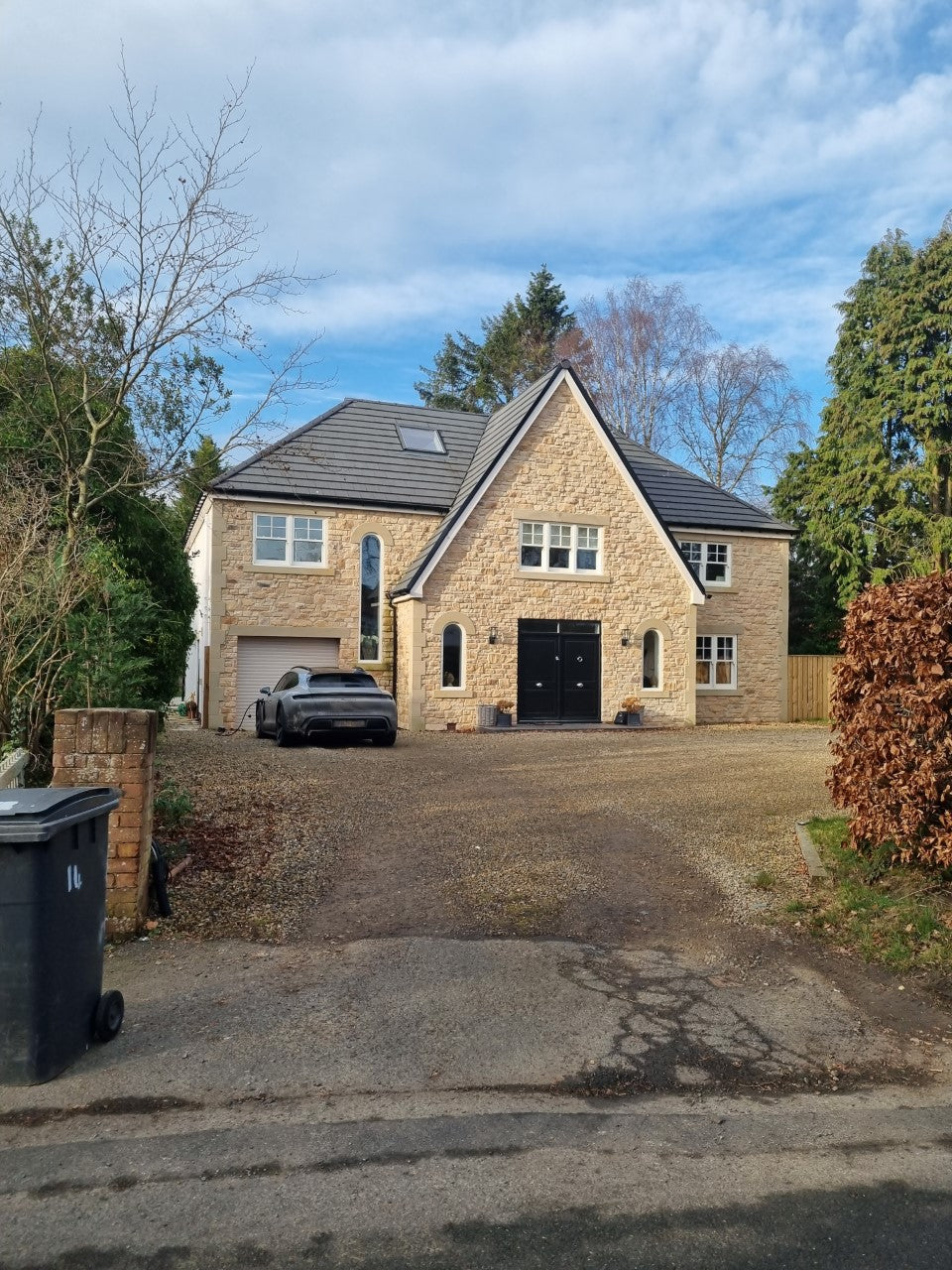 Modern home with stone cladding, large driveway, and surrounding trees on a clear day.