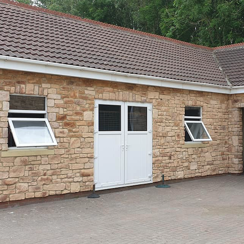 Cotswold Blend stone cladding on an exterior wall with white double doors and windows beside a paved area