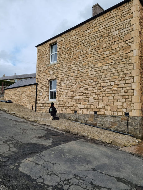 Exterior view of a building showcasing Burnt Buff Blend Stone Cladding with a worker preparing the area.