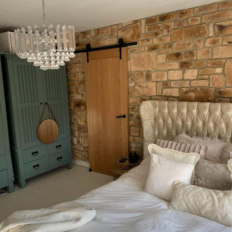 Cozy bedroom featuring rustic stone cladding wall, plush bedding, and elegant chandelier for a warm ambiance.