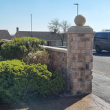 Stone cladding garden wall with decorative sphere and greenery in a residential setting.