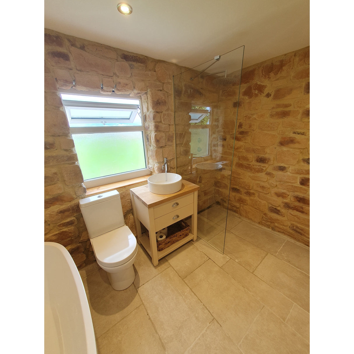 Modern bathroom featuring stone cladding walls, a glass shower, and elegant wooden furniture.