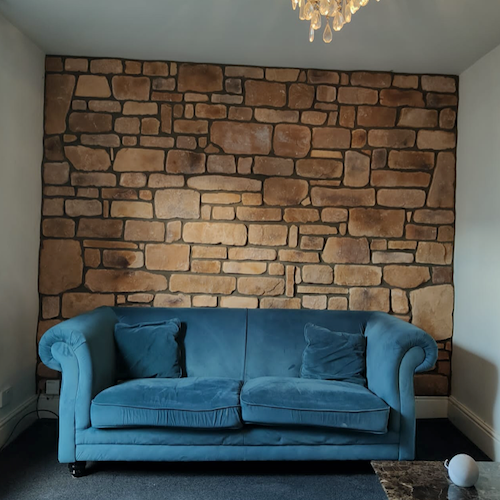 Living room featuring Cotswold Blend stone cladding wall behind a blue sofa, showcasing natural stone aesthetics.