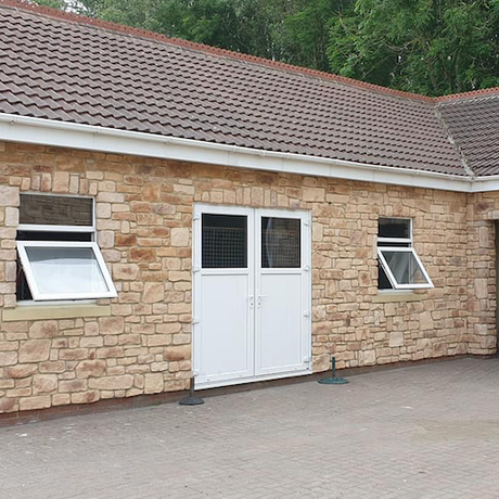 Exterior of a building featuring Cotswold Blend Stone Cladding with a white double door and adjustable window sashes.