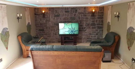 Living room featuring stone cladding wall, dark green sofas, and a TV, showcasing a cozy atmosphere with natural aesthetics.
