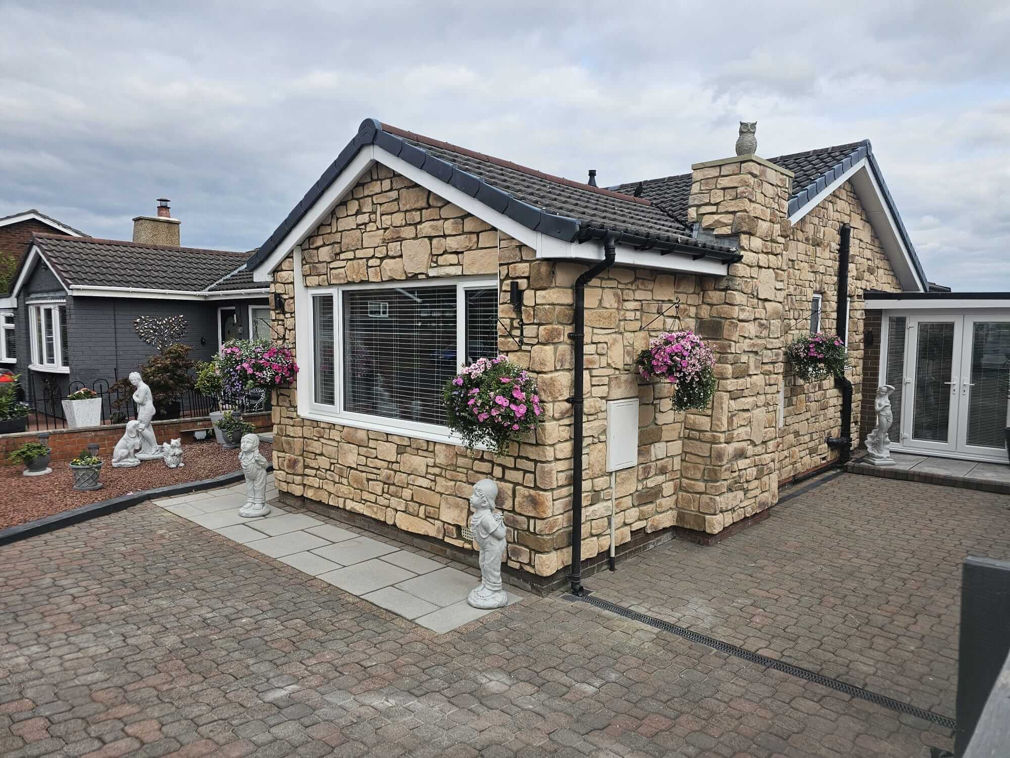 Stone-clad house exterior with flower pots and garden sculptures, showcasing beautiful Stone Cladding design.