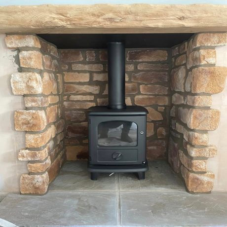 Modern wood stove nestled in a rustic stone-clad fireplace with a wooden mantel.
