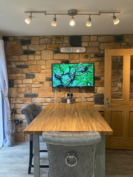 Interior view of a kitchen featuring Antique Blend Stone Cladding on the wall, a wooden dining table, and modern lighting.