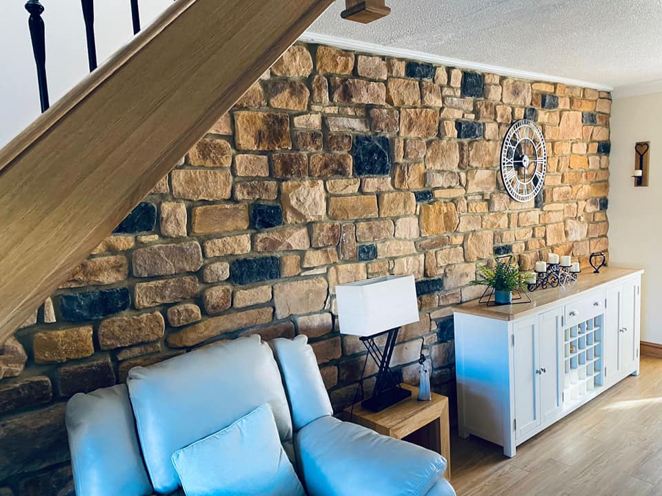 Interior view of a living room featuring antique blend stone cladding on a wall, with a couch and decorative items.