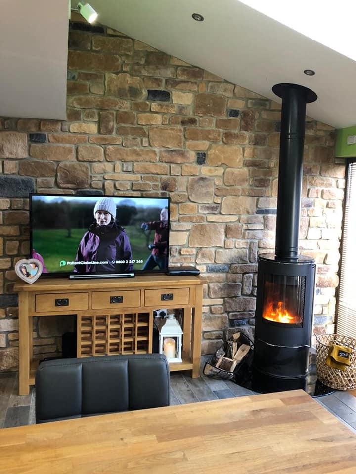 Living room with stone cladding wall, wooden furniture, television, and a cozy wood-burning stove.