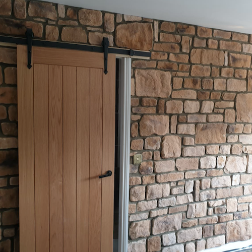 Interior view of a wooden sliding door beside natural stone cladding wall, showcasing rustic design and texture.