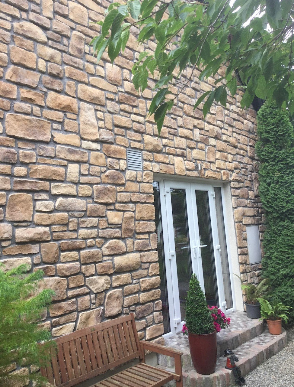 Stone cladding on a textured wall with a wooden bench and potted plants in a landscaped setting.