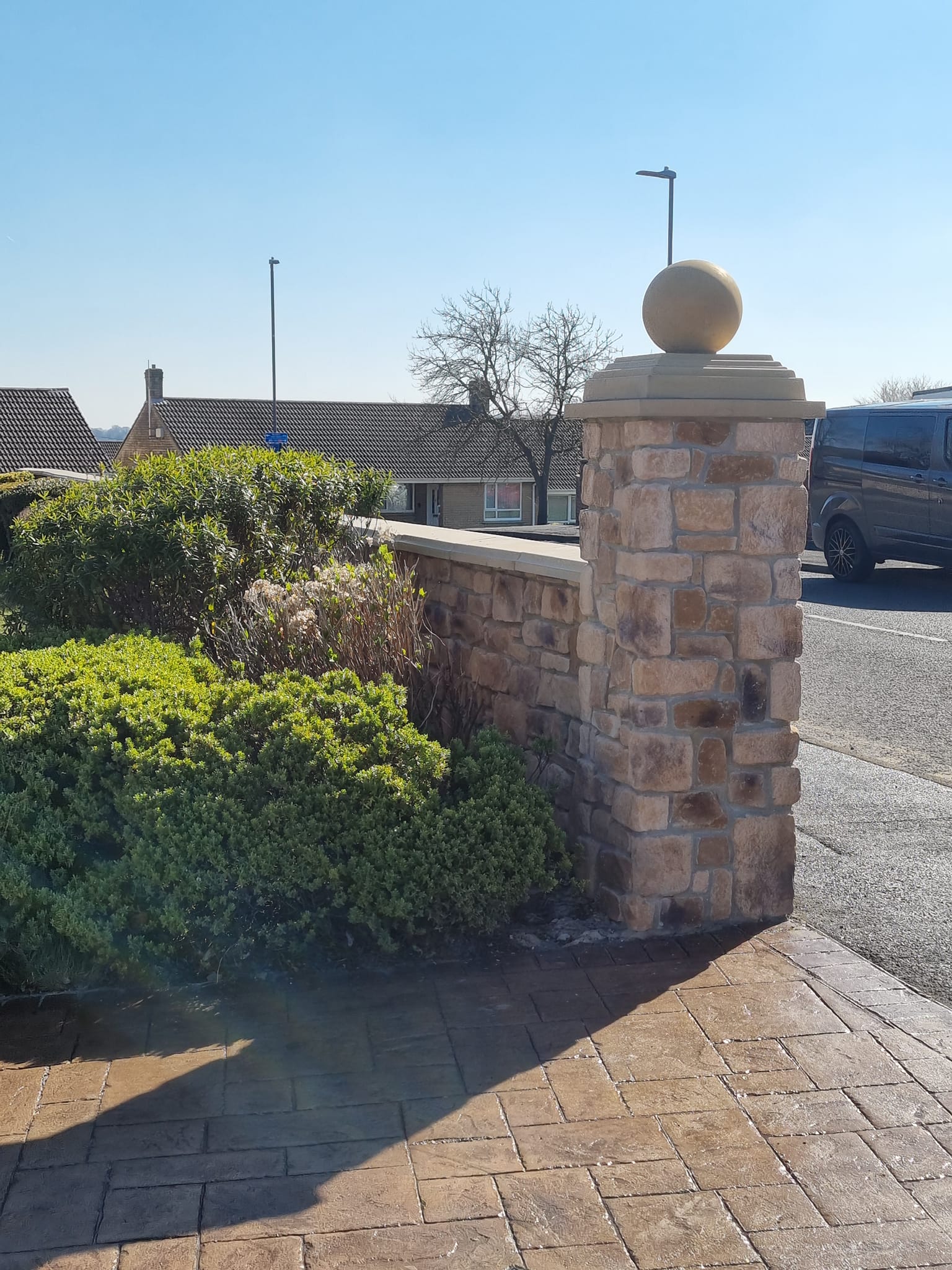 Stone cladding entrance with decorative sphere atop a stone wall, surrounded by greenery and a clear blue sky.