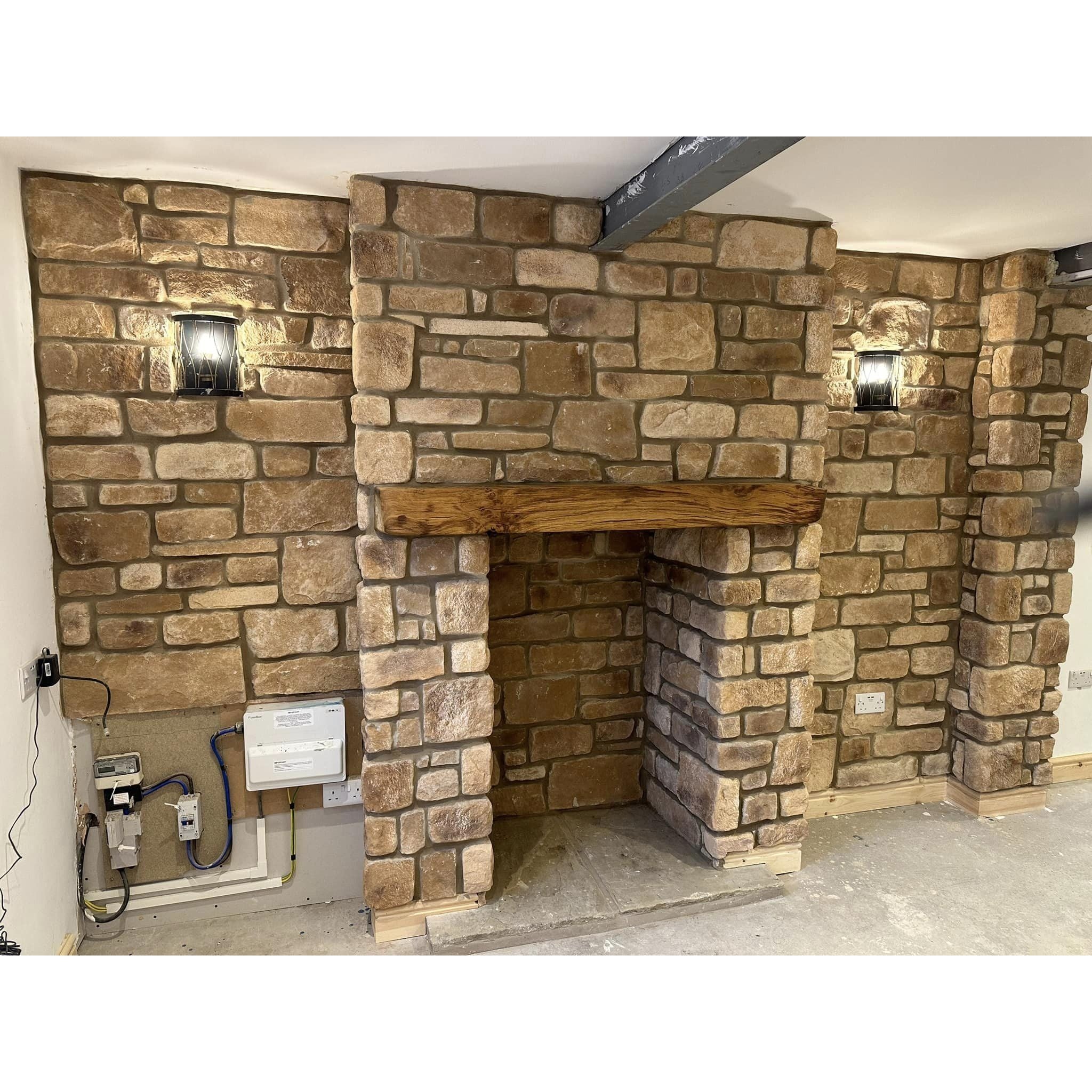Stone cladding installation in a cozy living space featuring Cotswold Blend stone slips and rustic wall lighting.