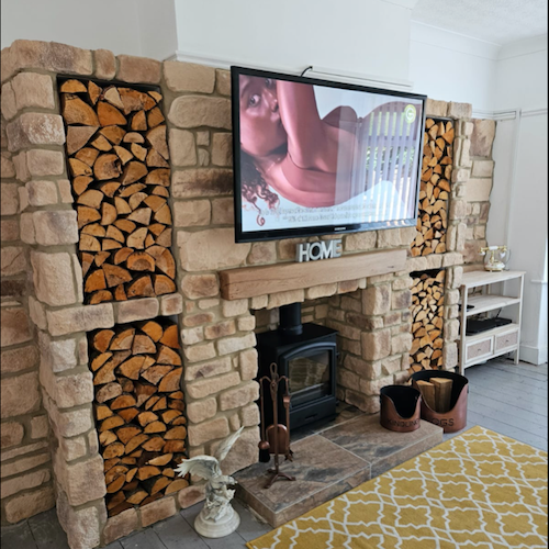 Cozy living room featuring a stone-clad fireplace with wood storage, complementing a modern TV setup.