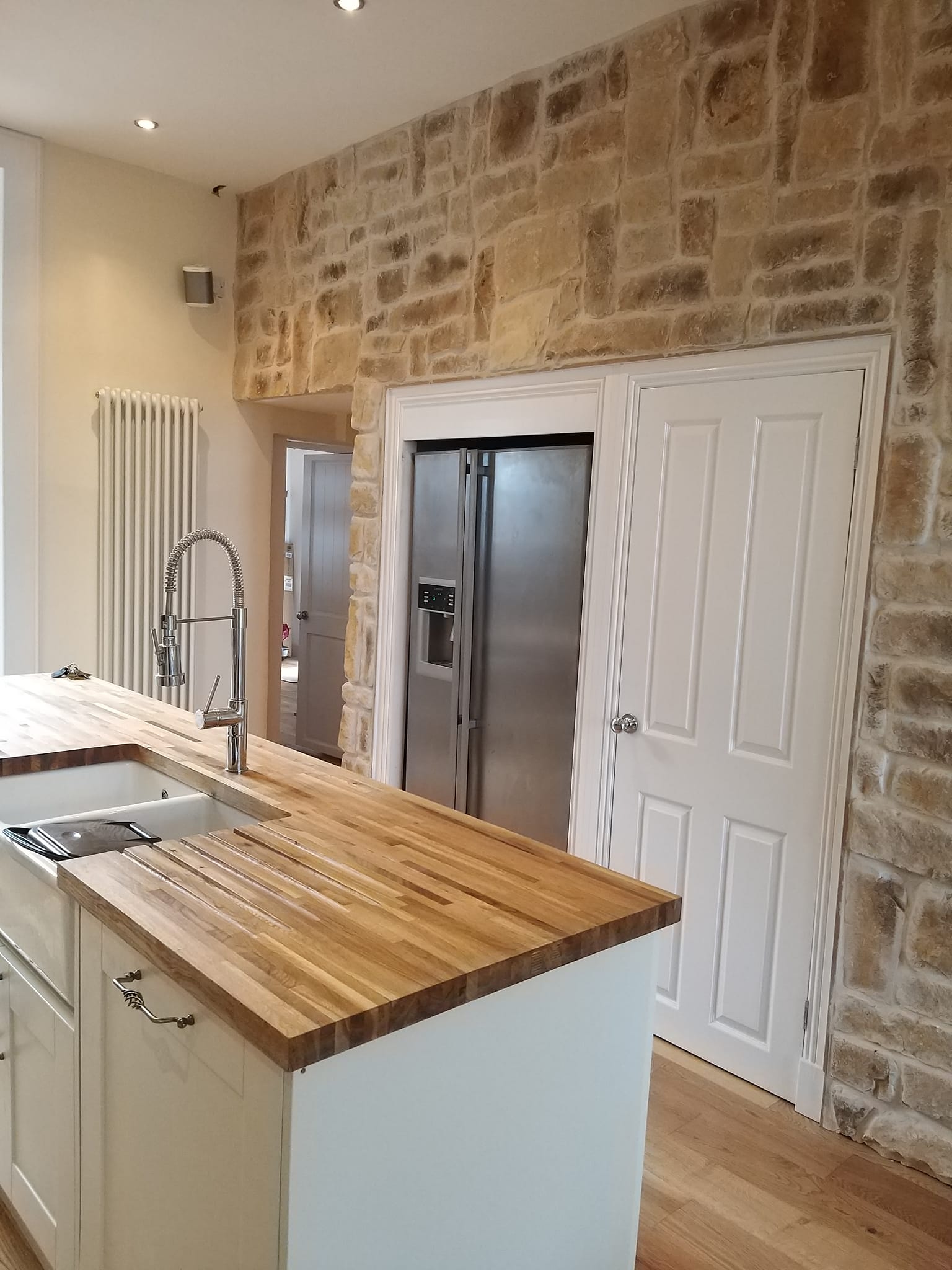 Modern kitchen featuring Cotswold Blend stone cladding on the wall and wooden countertop.