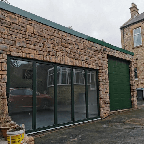 Stone Cladding facade on a modern building with large glass windows and a green garage door.