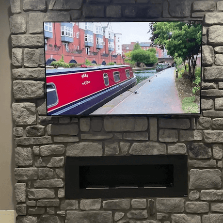Stone cladding wall featuring a TV above a modern fireplace with a view of a canal boat and urban surroundings.