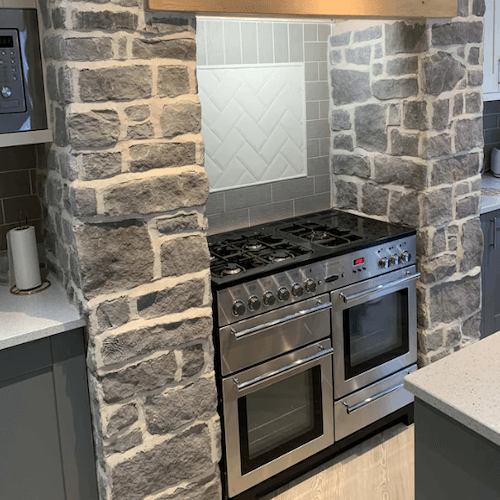 Stone cladding creating a rustic look around a modern kitchen range oven, highlighting light grey stone slips.