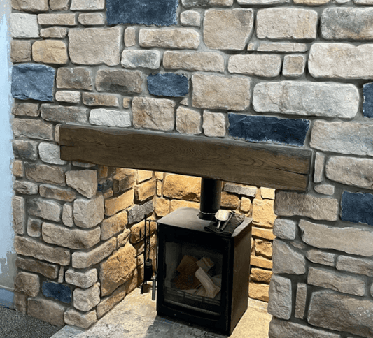 Rustic stone cladding wall with an oak mantel above a black wood stove, creating a cozy atmosphere.