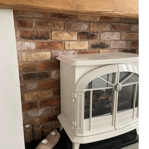 Mayfair Blend Brick Slips used as a stylish fireplace backdrop with a white stove and wooden mantel.