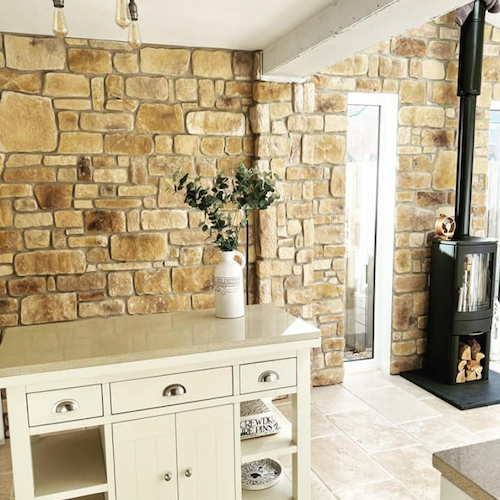 Interior view of a kitchen featuring Cotswold Blend stone cladding wall, modern furniture, and a wood-burning stove.