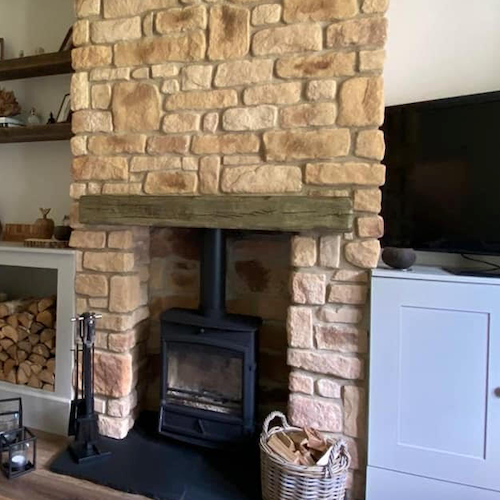 Stone cladding fireplace with a wooden beam and stove, showcasing natural aesthetics and warm tones in a cozy interior.
