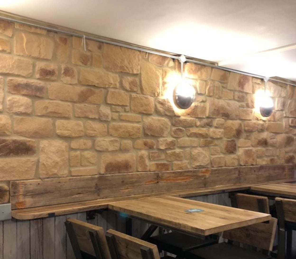 Interior view of a cozy restaurant featuring Burnt Buff Blend Stone Cladding on the wall with wooden tables.
